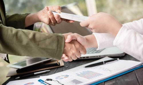 Business people shaking hands, finishing up meeting. businessman giving money to his partner while making contract - bribery and corruption concepts.